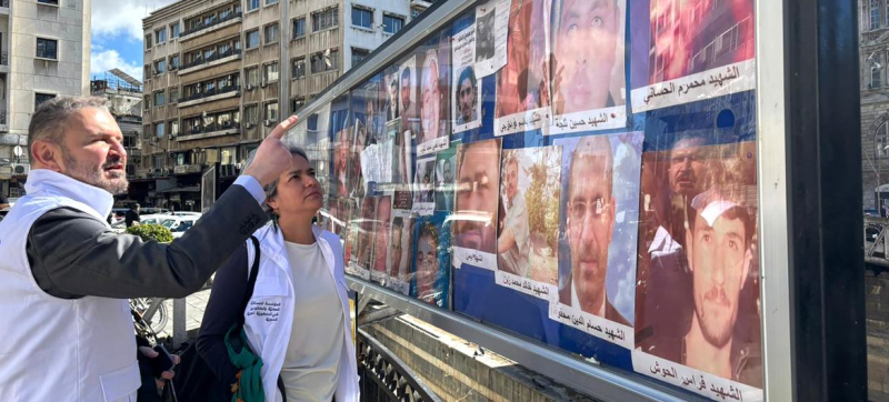 Карла Кинтана (в центре) посещает площадь Аль-Марджех в Дамаске, где семьи пропавших без вести выставляют фотографии в надежде найти своих близких.