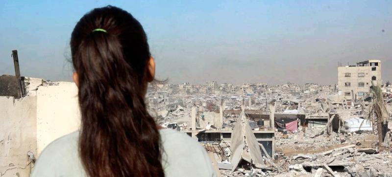 Девочка из Газы стоит на крыше своего поврежденного дома, глядя на разрушения по всему городу.